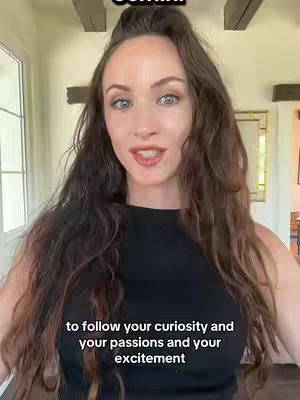 A medium shot of a woman with long brown hair standing in front of a light-colored interior. She's wearing a black top and speaking to the camera. Text overlays include the word 'Gemini' at the top and a statement about curiosity and excitement at the bottom.