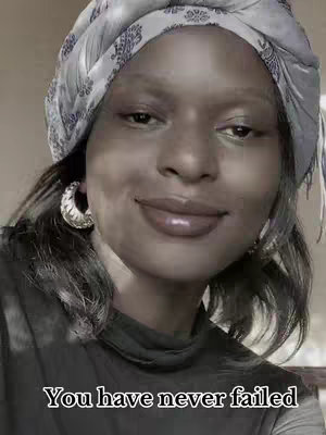 A close-up shot of a woman with dark skin wearing a headscarf. She is smiling slightly with full lips, and there are large hoop earrings. Text overlayed at the bottom.