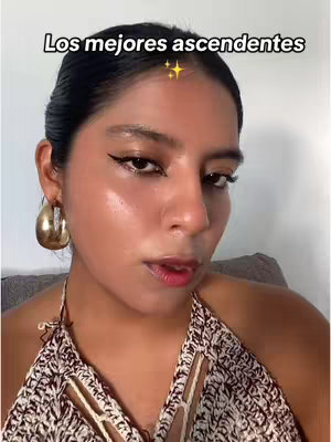 A woman with dark hair, wearing gold hoop earrings and a patterned halter top, looks at the camera. The text overlay says: Los mejores ascendentes, with a gold sparkle.