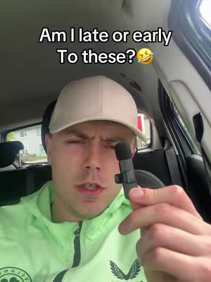 A man seated in a car holds a microphone, with text overlayed suggesting a question about being early or late. He wears a light green hoodie and a cap.
