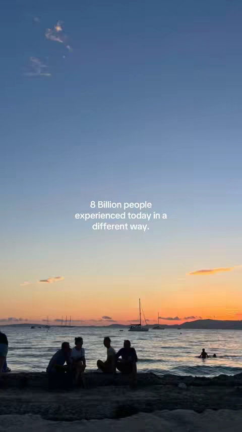A scenic image of a sunset over the ocean. Silhouetted figures are seated on a rock formation in the foreground, with sailboats in the distance. The sky transitions from blue to orange and yellow.