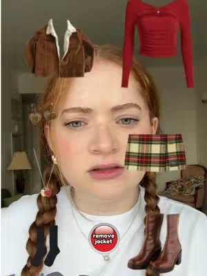 A young woman with reddish-brown hair styled in pigtails looks at the camera with a neutral expression. Various clothing items and accessories are laid out around her face, including a jacket, top, skirt, boots, socks, and earrings. A circular button labeled "remove jacket" sits near her neck.