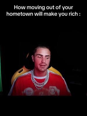 The cover image shows a man with a shaved head centered in the frame. Above his face, text reads: "How moving out of your hometown will make you rich :." The man wears a red shirt with a printed design on the front and two heavy silver chains. The background is solid black in the video, with a light source from the behind. The man appears to be looking at the camera and speaking.