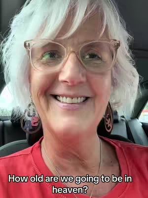 The cover image shows a close-up of a woman smiling broadly while sitting in a vehicle. She has short, white hair and is wearing large-framed glasses, through which her eyes are visible. She has on a red shirt and earrings. The text overlay at the bottom says 'How old are we going to be in heaven?'