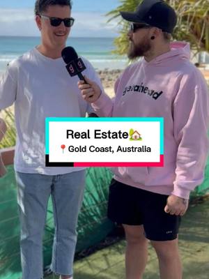 Two men are standing outside near a beach with clear sky. The man on the left is wearing sunglasses, a white t-shirt and jeans. The man on the right is wearing a black cap, sunglasses, and a pink hoodie, holding a microphone. A colored text box indicates the video topic.