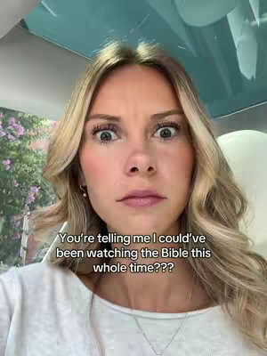 A woman with blonde hair and wide eyes is the main focus of the image. The background is blurred, showing some greenery and an interior that looks like a car. Text overlayed on the image reads, 'You're telling me I could've been watching the Bible this whole time???'.