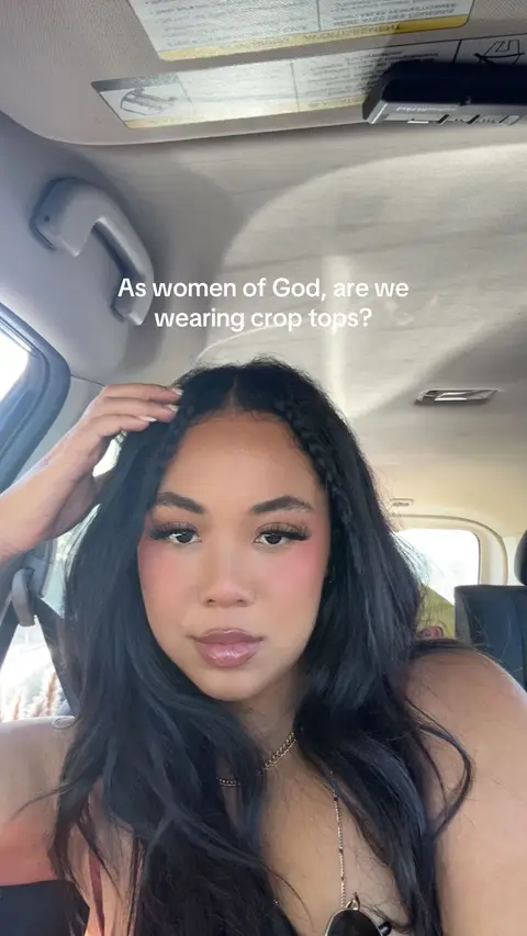 A woman with long black hair and makeup is inside a car, looking at the camera. Text is overlaid on the image.