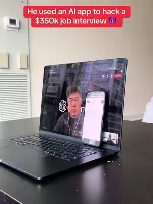 The cover image shows a laptop displaying a Zoom call with a person on the screen and a phone resting on the laptop screen. Text in a red banner at the top reads, "He used an AI app to hack a $350k job interview" with a devil emoji. The background is simplistic.