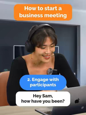 A woman with short dark hair wearing headphones is centered in the frame, smiling and looking towards a laptop. Text overlays appear in the form of colored rectangular speech bubbles with white text. Orange bubble with the text 'How to start a business meeting'. Blue bubble with text '2. Engage with participants'. White bubble showing the text 'Hey Sam, how have you been?' Background shows a simple office setting.