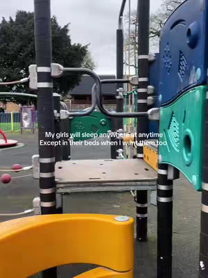 A person filming at a playground. The focus is on a play structure, with a view of the other playground equipment. The image is dominated by the play structure and includes text overlayed on the image. The mood reflected is casual and relatable, with neutral lighting and a cloudy sky.