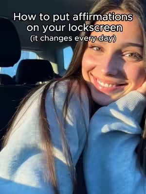 A woman with long brown hair smiles brightly, leaning on her hand while sitting in a car. The background shows a car interior.