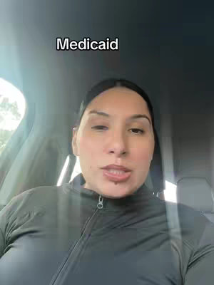 A woman is seated inside a car, with the focus on her face. She has dark hair and is wearing a black jacket. The text overlay reads 'Medicaid'.