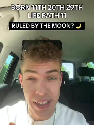 A selfie-style video cover image featuring a young man with short, textured hair, positioned inside a car. He has a slight smile and is looking at the camera directly. Above his head, a text overlay reads, "BORN 11TH 20TH 29TH LIFE PATH 11 RULED BY THE MOON?"