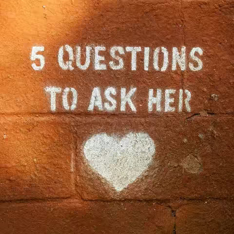 A close-up shot of a textured, reddish-brown brick wall. Stenciled in white paint are the words "5 QUESTIONS TO ASK HER" arranged over a roughly heart-shaped image also stenciled in white. The graffiti style suggests a raw and direct communication style.