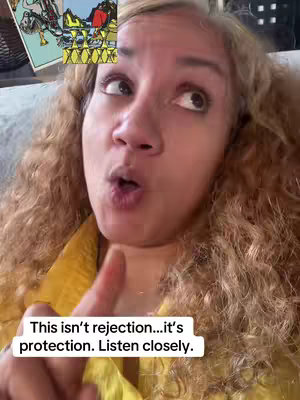 A close-up selfie of a woman with curly blonde hair, looking upward with a slightly surprised expression. She is wearing a yellow top and her index finger is pointing up. A small image of tarot cards is in the top left corner, and a text overlay is at the bottom.