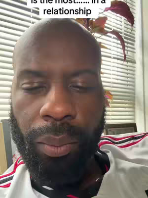 The cover image features a close-up shot of a bald, Black man looking downward with a neutral expression. The primary colors are neutral tones of skin and clothing. A plant with dark red leaves can be seen in the background near a window with vertical blinds.
