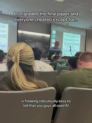 The image captures a classroom setting with a lecture in progress. A woman with blonde hair in a ponytail is shown from the back, sitting in a chair. In the center, a professor is visible, standing at the front of the classroom near a screen displaying text. The overall shot is filled with students in various casual outfits, suggesting a typical college environment. The lighting is bright, casting shadows and highlights across the room. The text overlay creates a humorous tone.