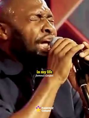 The image shows a man passionately singing into a microphone. He has sweat on his face, and his eyes are closed, suggesting deep emotion. Text overlays include a song lyric and a logo for 'FAMOUZ Gospel'. The background appears to be a stage setting with subtle lighting.