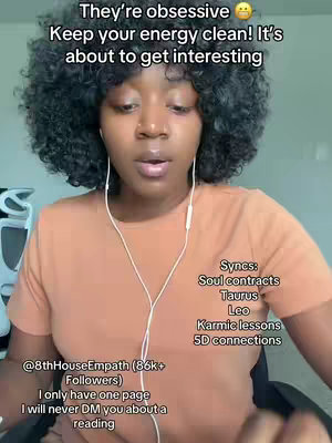 A woman with curly dark hair and an orange shirt is centered in the frame, looking towards the camera. She's wearing white headphones. The background is a plain, light-colored wall. Text overlays include phrases related to energy cleaning and a call for interest, with additional information about readings.