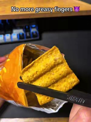 The image shows a close-up view of a person's hand holding a potato chip with black finger chopsticks. The chip is being pulled from an open bag. The background shows a dark surface. Above the image, there is an overlay of text.
