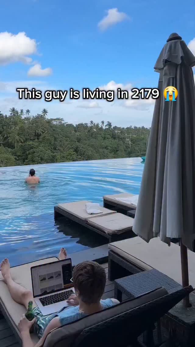 A person is seen reclining on a lounge chair next to a pool, with a laptop, a bottle, and a scenic background featuring a pool with someone in the water and lush greenery in the background. Text overlay indicating the video is from a futuristic setting.