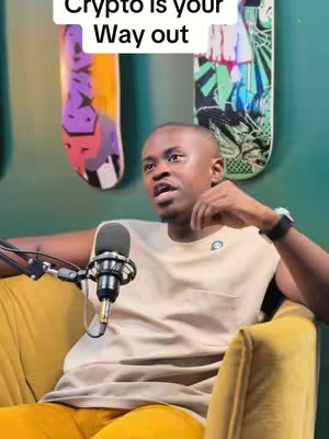 A man in a tan sleeveless shirt sits in a yellow chair, talking into a microphone. Behind him are two skateboard decks and a green wall. Text overlays say "Crypto is your Way out".