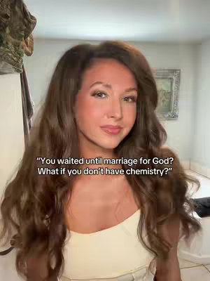 A woman with long brown hair and light makeup poses in front of a blurry background. She's wearing a neutral-colored top, and text overlays across the image, creating a contrast. The overall composition has a soft and inviting feel.
