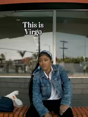 A woman, presumably the creator, is seated outdoors, possibly at a bus stop or similar seating area, with a background of a building and street infrastructure. Text overlayed on the image indicates the video's focus on the Virgo zodiac sign. The woman is wearing a denim jacket, a white undershirt, black pants, and a patterned headscarf. The overall color palette is natural with urban tones.