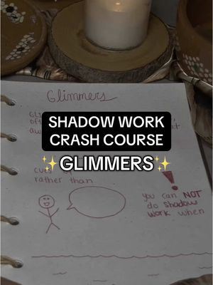 The cover image is a vertical shot of a notebook page. Handwritten text at the top reads 'Glimmers'. A black rectangular box in the center states 'SHADOW WORK CRASH COURSE' with 'GLIMMERS' below. A stick figure is drawn to the left of the text. A candle in a wooden holder sits above the page and various items can be seen faded in the background.