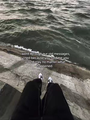 The image shows a first-person perspective of someone's legs and feet, with black pants and white and black sneakers resting on a concrete surface. Beyond this, a body of water with waves and a cloudy sky fill the backdrop. Text overlayed on the image reads, 'i went through our old messages; i cried because you told me you would stay no matter what happened.' evoking feelings of heartbreak, betrayal, and dwelling on past promises.