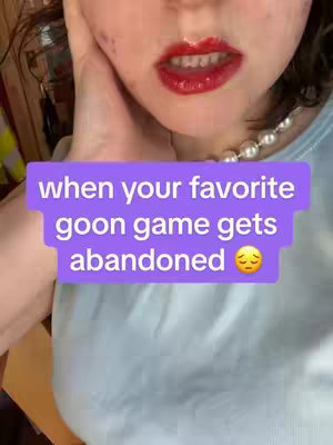 Close-up shot of a person's face, focusing on the lower face. Red lipstick is visible on the lips which are slightly parted. A pearl necklace is visible. Overlayed on the shot is a text box containing the text: 'when your favorite goon game gets abandoned' with a sad face emoji.
