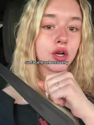 A young woman with blonde hair is in a car, looking at the camera. Overlayed text reads \"surface level recovery\". The lighting is natural, with a soft focus on the woman's face.