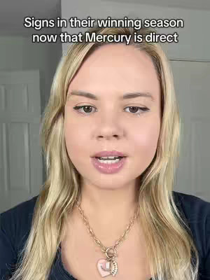 A medium shot focuses on a woman with long blonde hair, fair skin, and a gentle smile. She wears a dark top and a necklace with a heart pendant. The background is neutral with a subtle white interior. Over her head is text that contains a message related to astrological signs in their winning season.