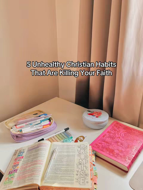 A well-lit shot featuring a white desk in a corner setting. On the desk, there's an open Bible with colorful tabs, a closed pink floral-patterned book, a pencil case with markers, and a small, floral-decorated container. The background features a soft, neutral-toned wall and curtains.