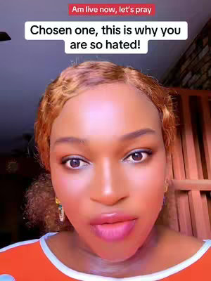 A selfie-style video cover image featuring a woman with light orange hair styled with waves. Above her, a red bar reads "Am live now, let's pray," while the main text overlay says, "Chosen one, this is why you are so hated!" The woman has a close-up face, with emphasized makeup and a strong gaze.