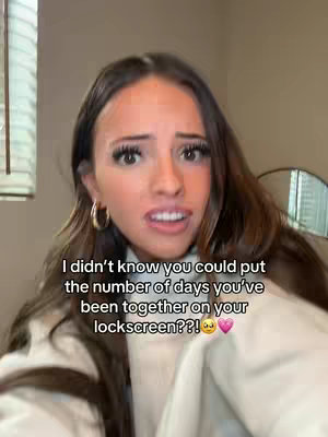 A selfie-style shot of a woman with brown hair, wearing a cream-colored sweater. She has a surprised expression, with her mouth slightly open. Text overlayed on the image says, I didn't know you could put the number of days you've been together on your lockscreen??