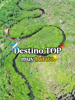An aerial view of a winding river with lush green vegetation on either side. Text overlays read 'Destino TOP muy barato'. An airplane illustration and a flag icon are also present.