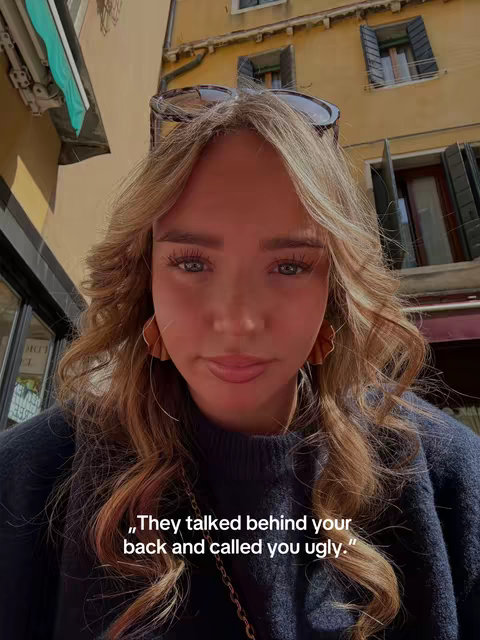 A young woman is shown in a close-up, angled slightly upwards within a sunlit outdoor setting, likely a European city. The background features a yellowish building with several windows and window treatments. The woman has long, wavy blonde hair and is wearing a dark blue sweater. Stylish sunglasses rest atop her head. A quote is superimposed on the image, written in a serif typeface.