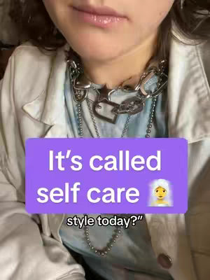 The cover image features a person, likely a female, with a close-up of her face and upper chest. She is wearing a light-colored jacket over a patterned top. A bold, silver necklace with chain links and charms is prominently displayed around her neck. A rectangular, purple text overlay with white text dominates the lower center of the image.