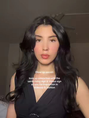 A woman with long, wavy dark hair and fair skin is centered in the frame, looking towards the camera. She has full lips and is wearing a black top. Text in a white sans-serif font overlays the image, offering a beauty tip about astrology and makeup.