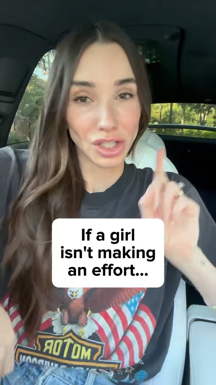 The cover image is of a woman in a car, angled from the chest up. She is in the driver's seat, with the car interior in the background. She is looking directly at the viewer, with her right index finger raised as if making a point. A text overlay on a white rectangular background partially obscures her torso. Her long brown hair is down. She is wearing a black t-shirt with a graphic of an eagle and the American flag on it. Some trees and the open road can be seen through the car window.