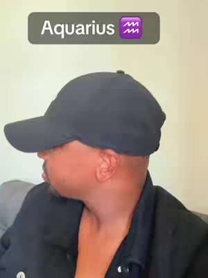 A man wearing a black cap and jacket is captured from the side, looking towards the left of the frame. Above him is a dark gray rectangle with the word 'Aquarius' in off-white text, and an Aquarius zodiac symbol.