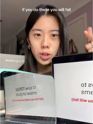 A young woman with dark hair is centered in the shot, looking directly at the camera with a neutral expression. She is holding up two laptops that display text. The background is a blurred room setting.