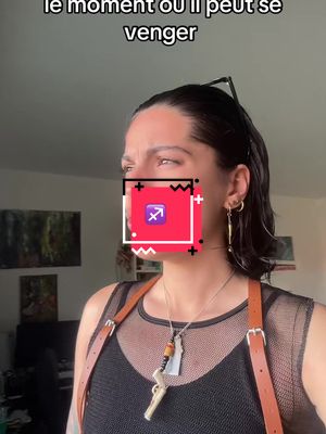 A woman with dark hair is facing right and looking slightly away from the camera. Overlayed on her face is a red, black and white square with a Sagittarius symbol. She is wearing a black tank top and a brown harness-like strap. There is text in upper left corner.
