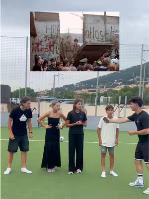 The image showcases a montage with two distinct layers. The top layer presents a black-and-white, historical photo depicting a scene at the Berlin Wall. The bottom layer features a group of six young people standing on a green playing field, with a soccer ball in the foreground. The people are dressed in casual clothes, suggesting a contemporary setting. The composition combines historical and modern elements.
