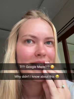 A close-up shot features a woman with blonde hair, lightly styled back, and fair skin. She is looking towards the right with a partially open mouth, appearing surprised. Text overlays are present, including 'Tf?! Google Maps?!' and 'Why didn't I know about this,' accompanied by emoji. Her left hand is near her mouth and she is also wearing a ring. The background is blurred but the window frame and ceiling is visible.
