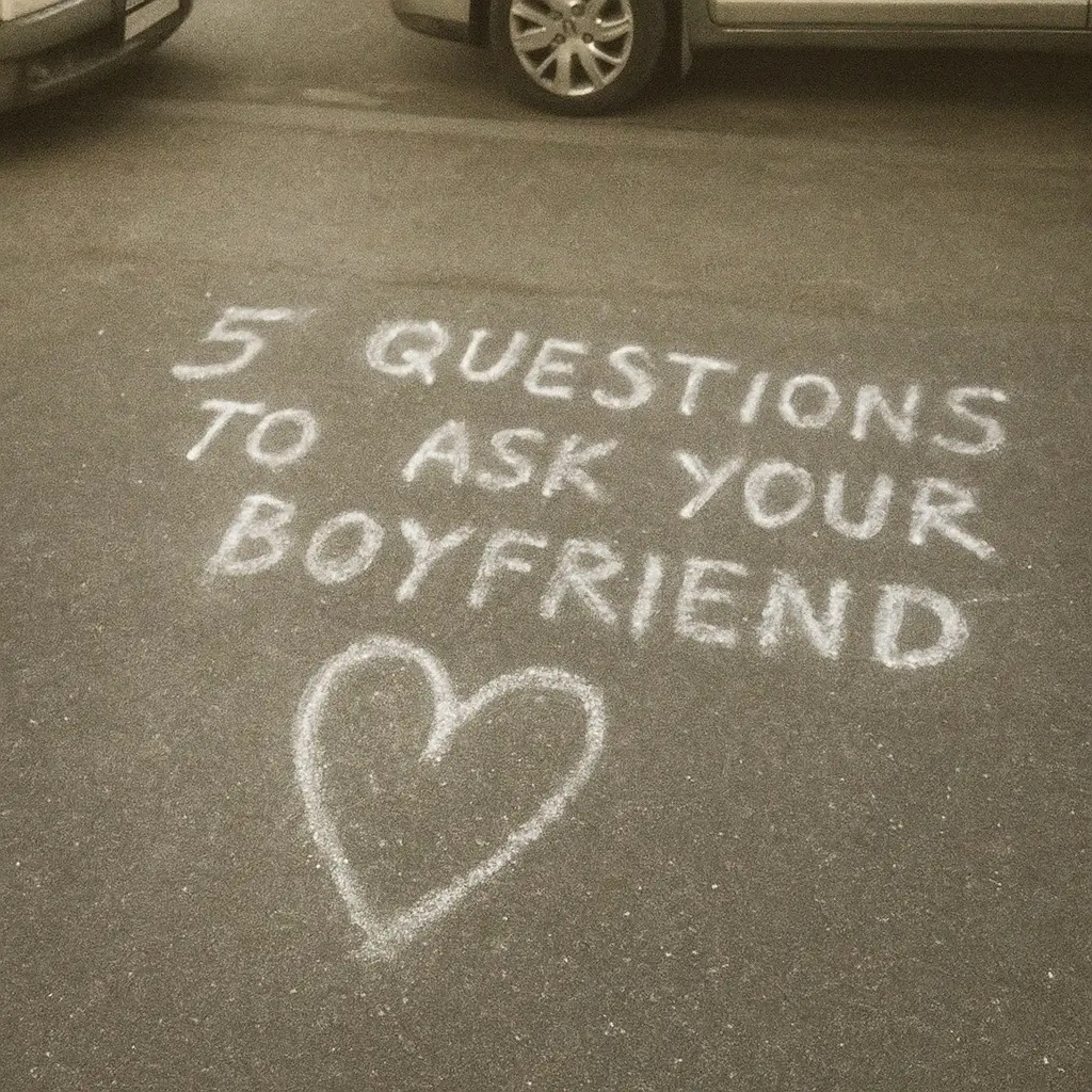 An image taken from a high angle directly above the pavement. The pavement is a muted gray with textures. In the center, chalk is used to write the text '5 QUESTIONS TO ASK YOUR BOYFRIEND,' with the words positioned in three lines. Below the text is a heart drawn with chalk. To the upper portion of the image, partially visible, are two vehicles.