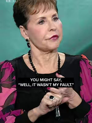 A medium shot shows a woman with short, dark hair and a dark top. She is wearing a black beaded necklace and earring and a ring. Text overlays a black box with white font over the bottom part of the image.