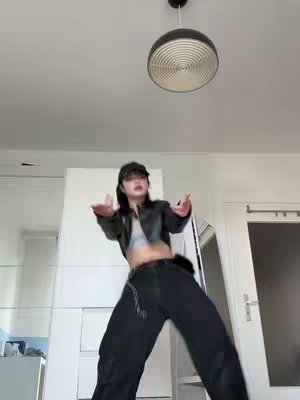 The cover image shows a woman in a dance pose in an interior lit by a ceiling lamp. She wears a black cap, jacket, and pants with her arms outstretched. The background includes a white wall/closet and a doorway.