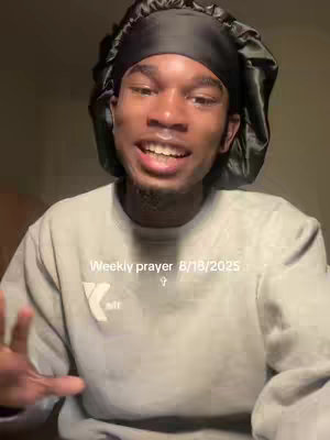 A medium shot shows a young Black man with a subtle smile, looking directly at the viewer. He is wearing a light gray sweatshirt and a black satin head covering. The background is poorly lit, with warm tones suggesting an indoor space. Text in white reads "Weekly prayer 8/18/2025".
